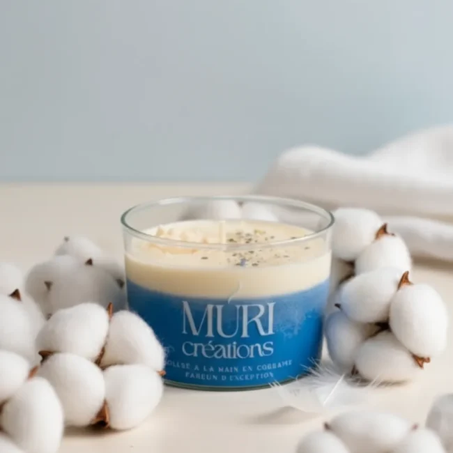 Bougie parfumée à la fleur de coton de la marque artisanale Muri Créations, présentée dans un pot en verre avec une cire bicolore blanche et bleue, entourée de fleurs de coton douces.