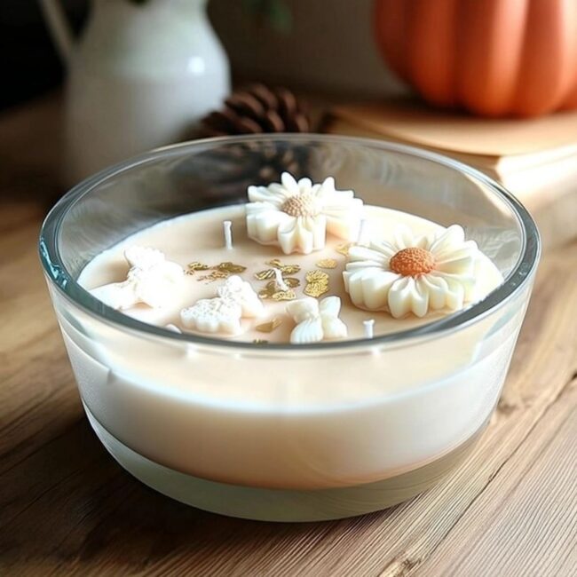 À propos 8 Bougie artisanale XXL 800ml avec fleurs blanches, papillons en cire et feuilles d’or, dans un verre rond sur une table en bois