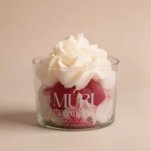 Bougie gourmande parfumée à la cerise noire de la marque artisanale Muri Créations, présentée dans un verre transparent avec une cire fouettée blanche façon chantilly et des inserts rouges imitant un dessert fruité.