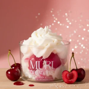 Bougie gourmande parfumée à la cerise noire de la marque artisanale Muri Créations, présentée dans un verre avec une cire fouettée blanche façon chantilly et des inclusions rouges, entourée de cerises fraîches sur un support en bois.