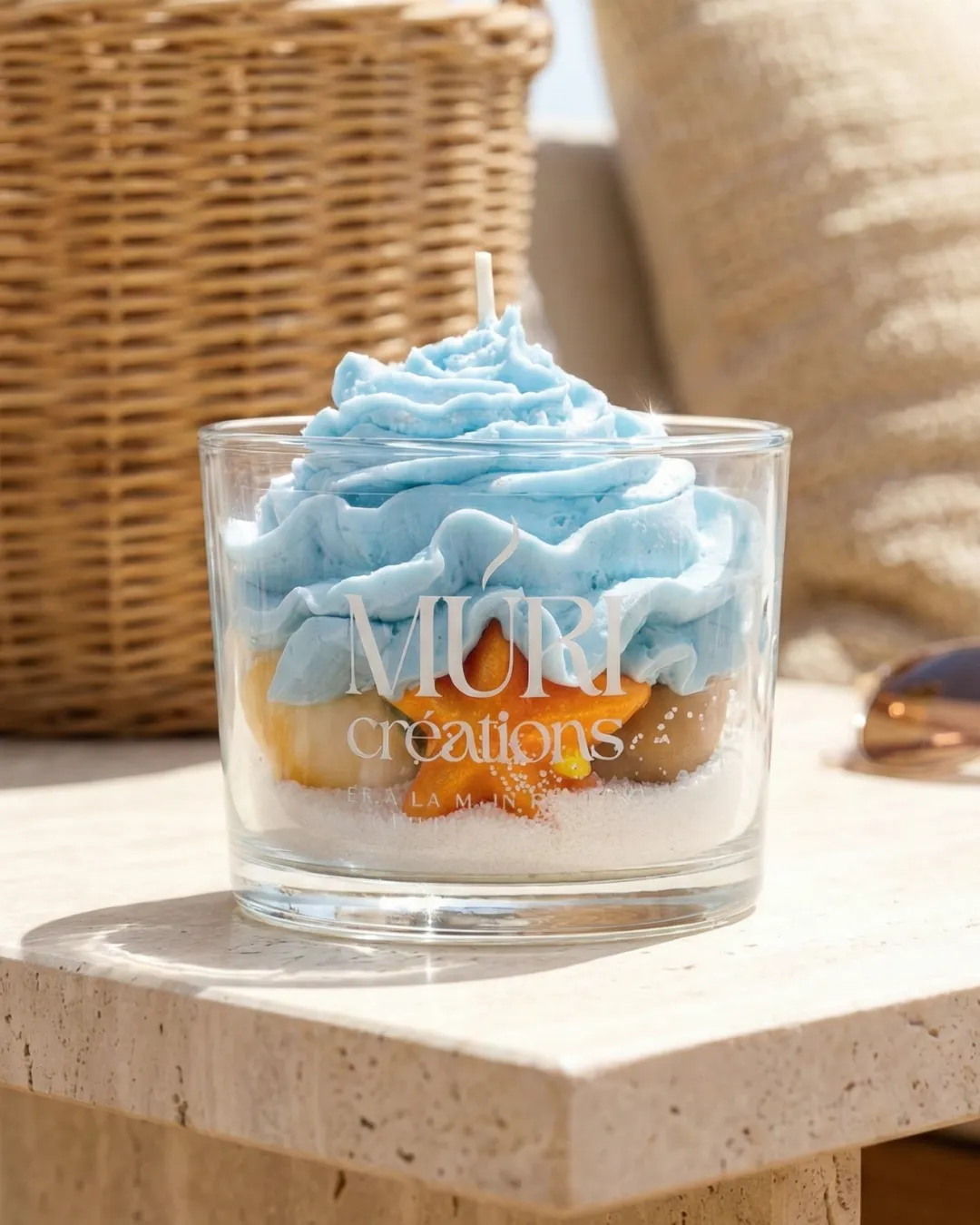 Bougie 150ml - BRISE MARINE 1 Bougie artisanale gourmande Brise Marine de la marque Muri Créations, collection printemps-été 2026. Bougie décorative en verre avec cire effet sable, étoile de mer orange et topping chantilly bleu océan.