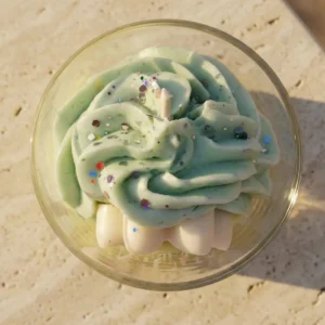 Vue de dessus d'une bougie artisanale Muri Créations au parfum floral de jasmin, disposant d'une cire fouettée verte pailletée style chantilly dans un verre, issue de la collection printemps été 2026.