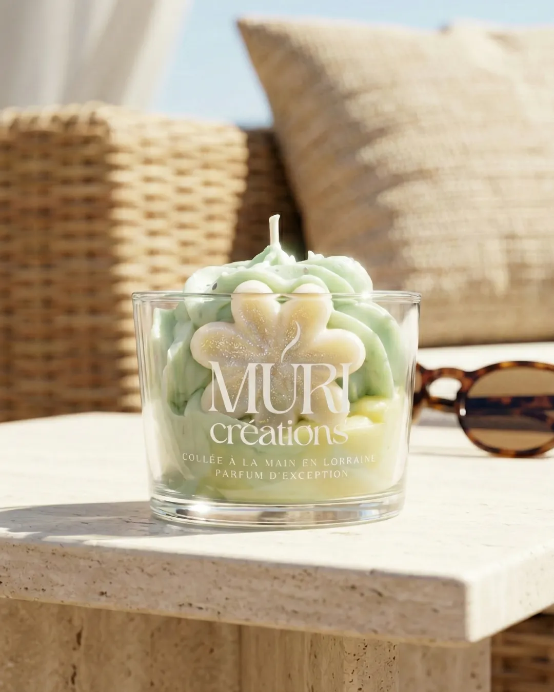 Bougie 150ml - JASMIN 1 Bougie artisanale au parfum floral de jasmin de la marque Muri Créations, collection printemps été 2026. Gros plan sur une bougie gourmande en verre avec cire fouettée vert pastel et insert fleur, coulée à la main en Lorraine, posée sur une table en pierre au soleil.
