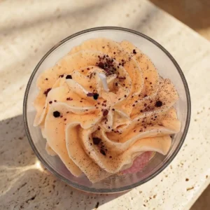 Vue de dessus d'une bougie artisanale parfum Litchi à la cire fouettée couleur pêche et paillettes, issue de la collection printemps été 2026 de la marque Muri Créations.