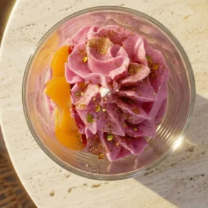 Vue de dessus de la bougie artisanale parfum Monoï Passion de la marque Muri Créations. Cette bougie gourmande de la collection printemps été 2026 présente une cire fouettée rose style chantilly, saupoudrée de paillettes dorées et agrémentée de décors fruités jaunes dans un contenant en verre.