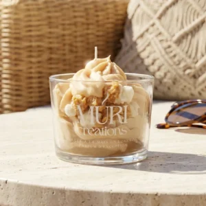 Bougie artisanale gourmande au parfum popcorn de la marque Muri Créations, issue de la collection printemps été 2026. Cette bougie en verre présente une cire fouettée beige façon chantilly, coulée à la main en Lorraine, posée sur une table en pierre dans une ambiance estivale et ensoleillée.