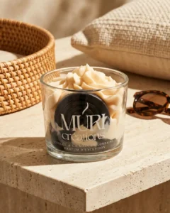 Accueil 5 Bougie artisanale Muri Créations au parfum réglisse, issue de la collection printemps été 2026. Cette bougie gourmande coulée à la main en Lorraine présente une cire effet chantilly beige et un insert noir en forme de rouleau de réglisse, posée sur une table en travertin dans une ambiance estivale ensoleillée.