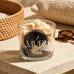 Bougie artisanale Muri Créations au parfum réglisse, issue de la collection printemps été 2026. Cette bougie gourmande coulée à la main en Lorraine présente une cire effet chantilly beige et un insert noir en forme de rouleau de réglisse, posée sur une table en travertin dans une ambiance estivale ensoleillée.
