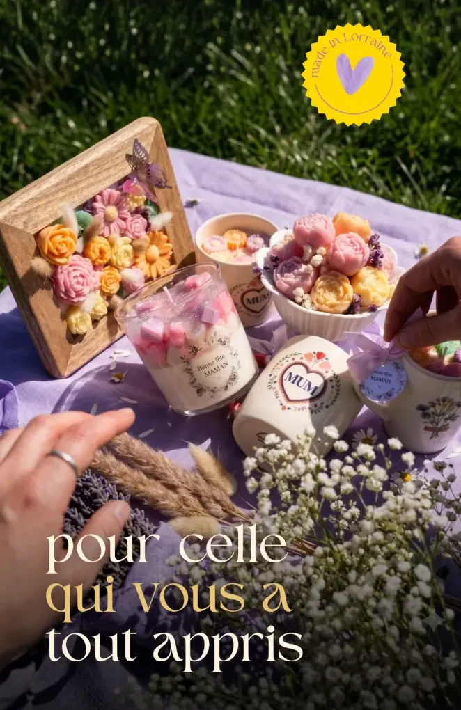 Accueil 1 Collection Fête des Mères par Muri Créations : assortiment de bougies et fondants artisanaux en forme de fleurs sur une nappe violette. Idée cadeau fait main en Lorraine avec tasses Mum et bougies Bonne fête Maman en plein air.