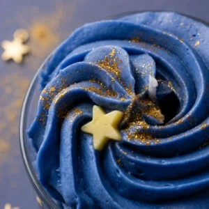 Gros plan sur la cire bleue fouettée de la bougie artisanale Nuit Étoilée par Muri Créations, décorée de paillettes dorées et d'une étoile. Parfum au bois de santal, ambre et notes florales.
