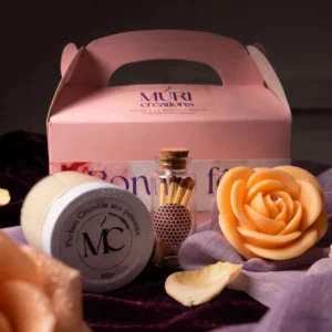 Coffret cadeau Fête des mères Muri Créations comprenant une boîte rose, une bougie en pot parfum crumble aux pommes, une bougie sculptée en forme de rose et une fiole d'allumettes sur un tissu velours prune.